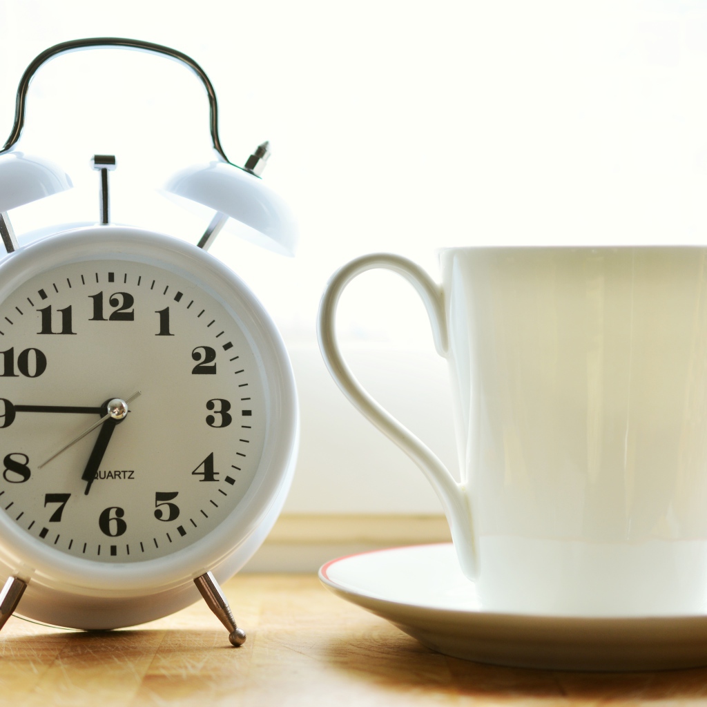 Белый будильник и чашка кофе на утреннем столе