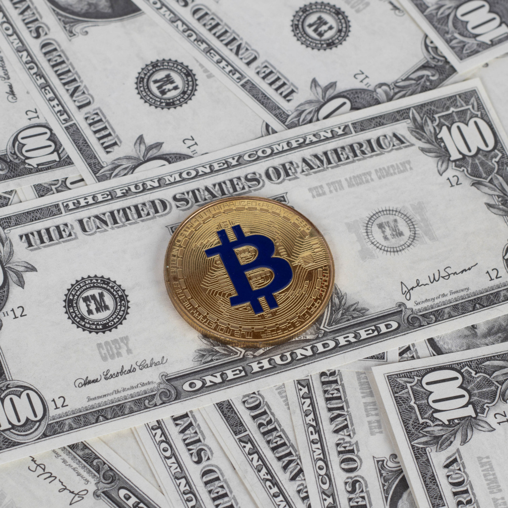Монета Биткоин лежит на стодолларовых купюрах