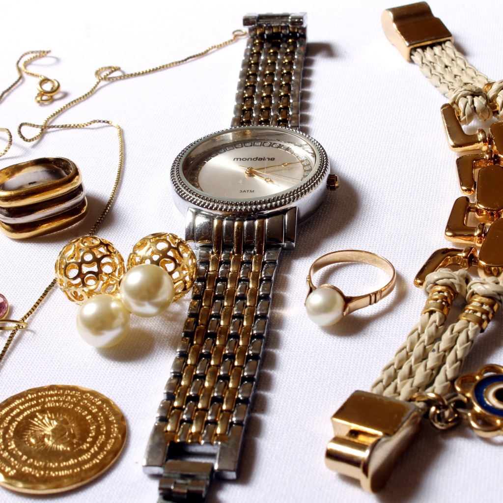 Wrist watch and gold jewelry on white background