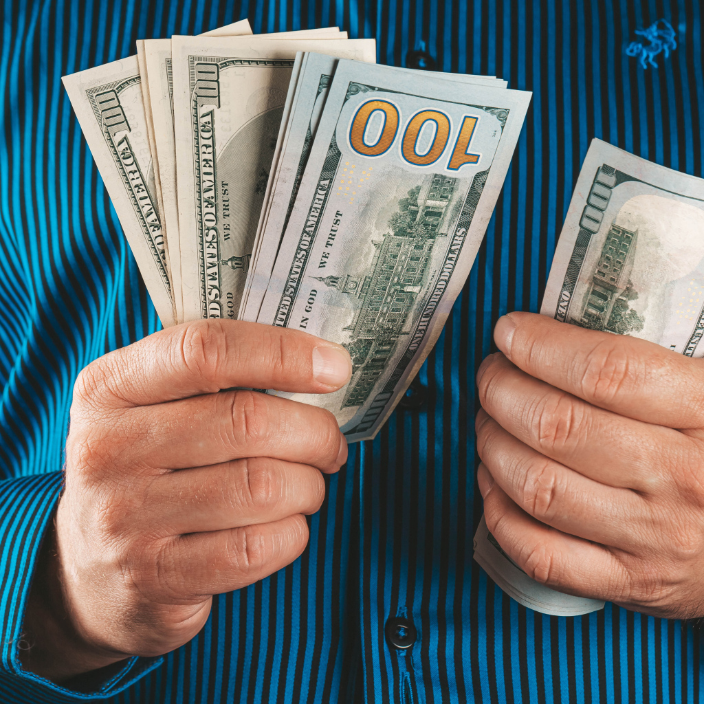 Мужчина считает сто долларовые купюры 