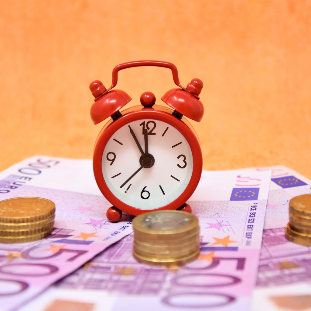 Маленький красный будильник с купюрами евро и монетами