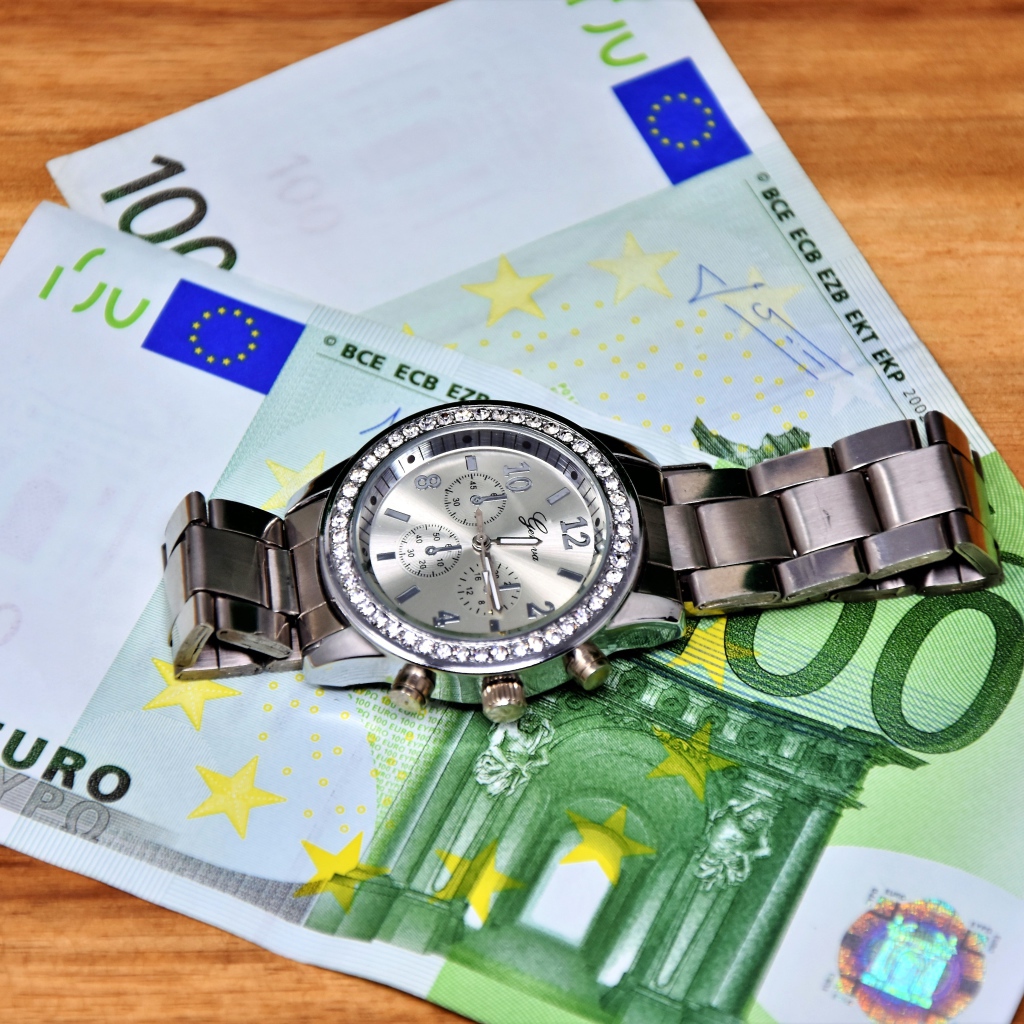 Две купюры по сто евро с часами на столе 