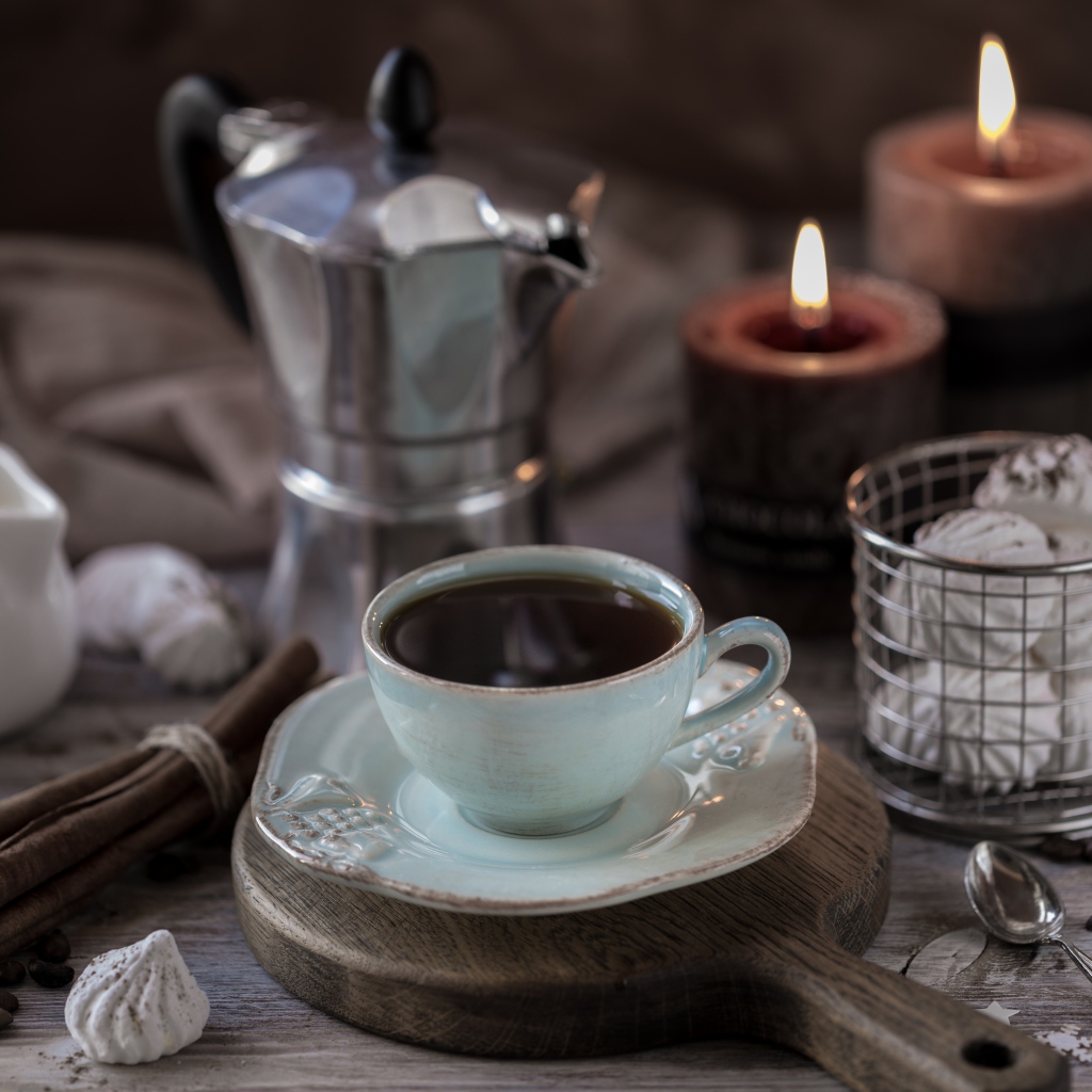 Чашка эспрессо на столе с корицей, зефиром и зажженными свечами