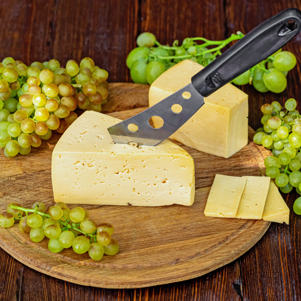 Кусок твердого сыра на столе с ножом и белым виноградом