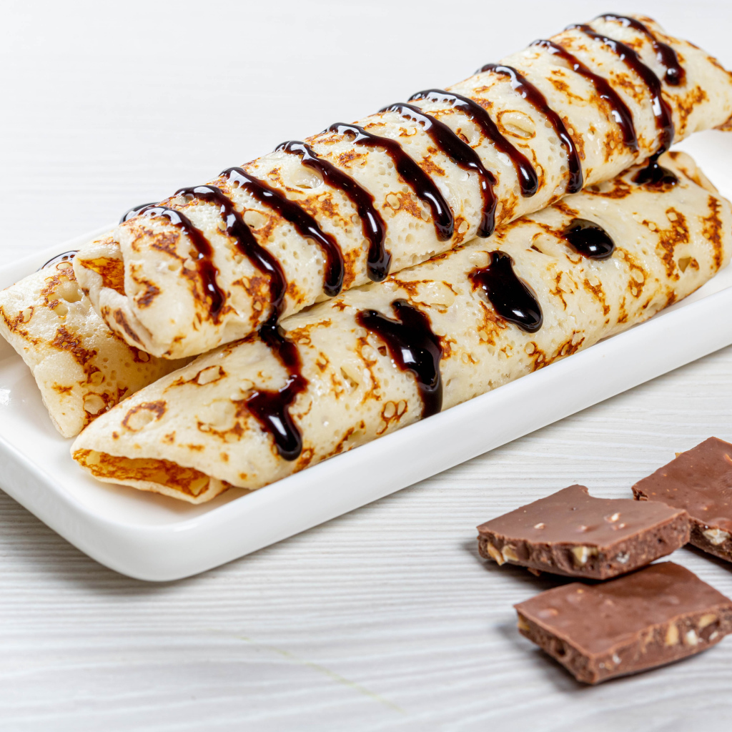 Аппетитные тонкие блины на белой тарелке с шоколадом