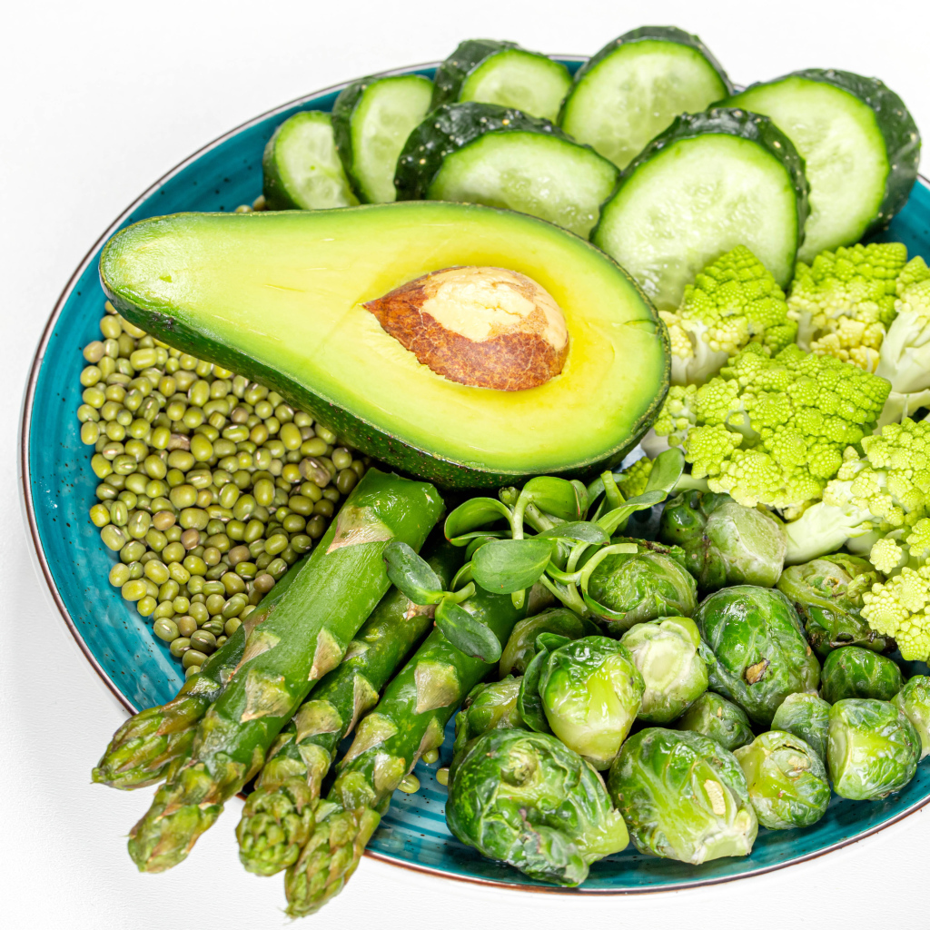Авокадо, капуста, огурцы и спаржа на тарелке на белом фоне