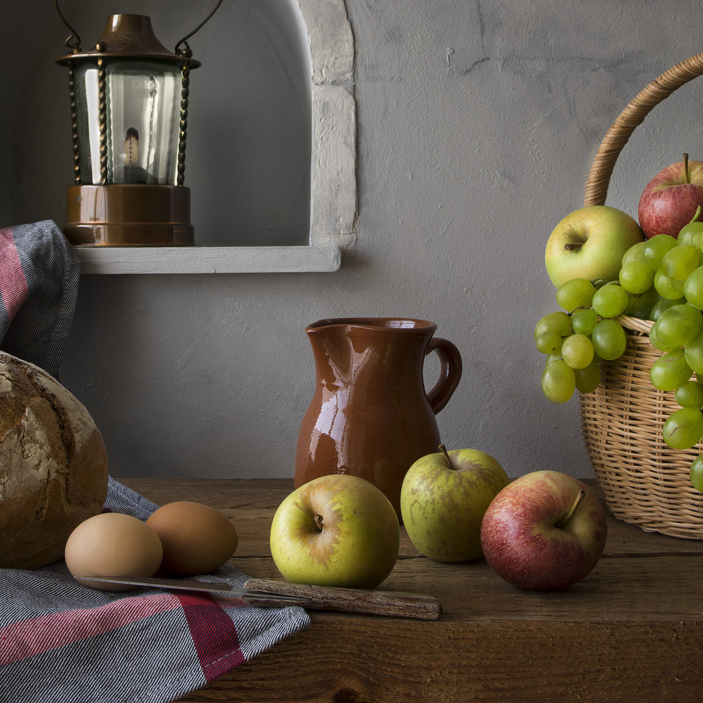 Корзина с яблоками и виноградом на столе с хлебом и яйцами