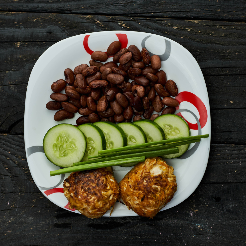 Фасоль на тарелке с оладьями и огурцами 