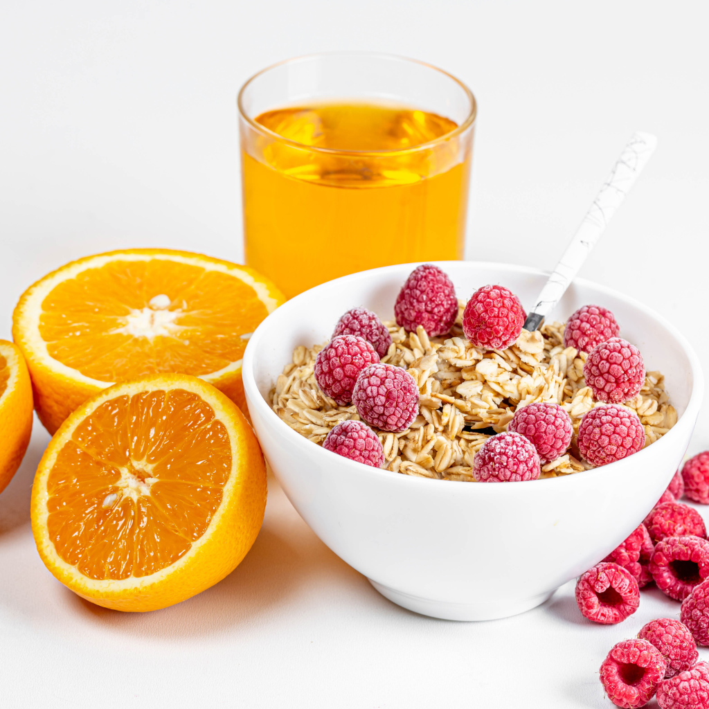 Миска мюсли с ягодами малины и апельсинами на столе с соком