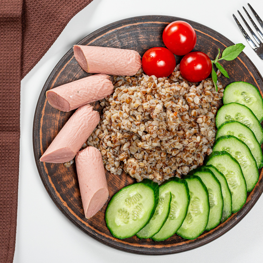 Гречка на тарелке с помидорами, огурцами и сосисками