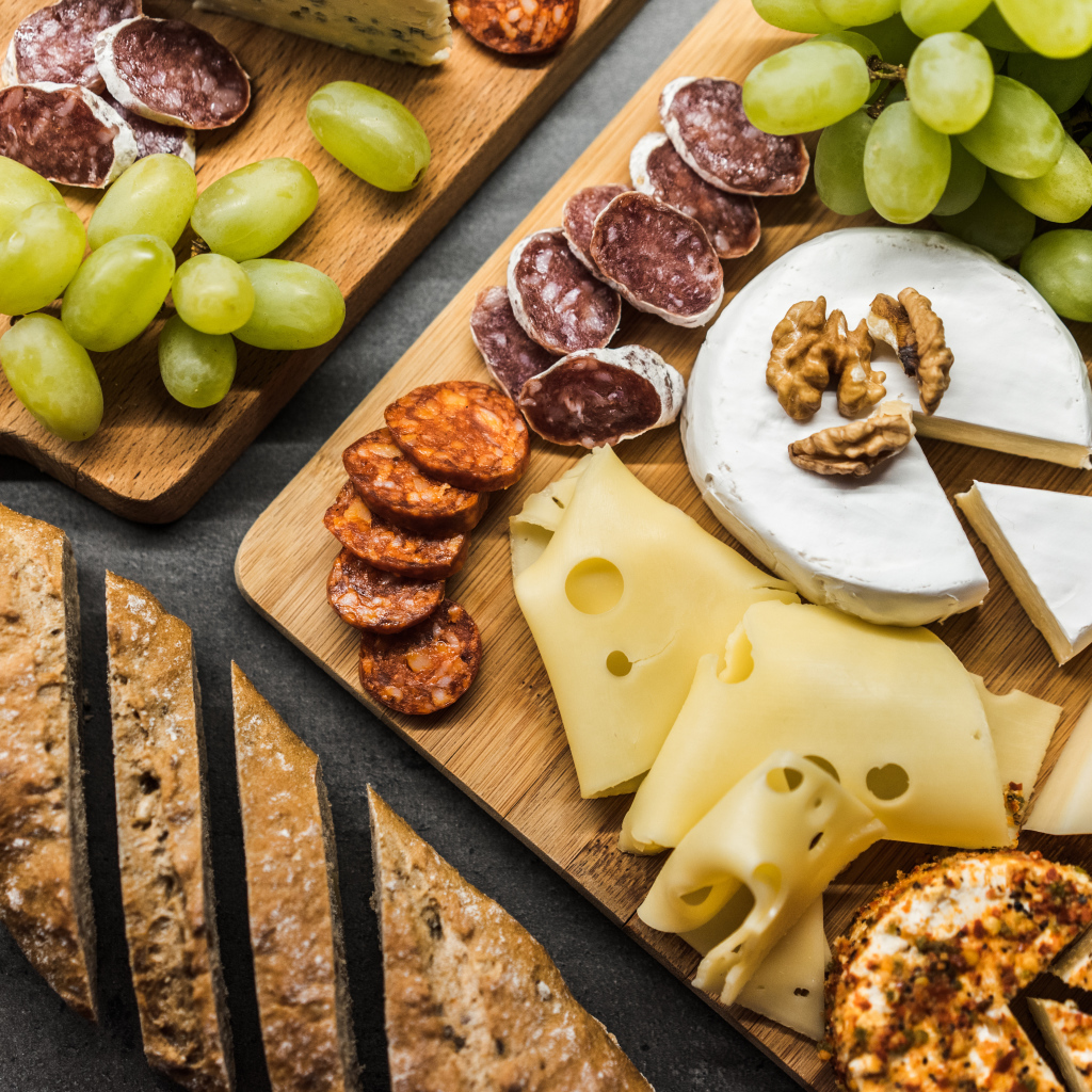 Сыр, колбаса, виноград и батон  на столе 