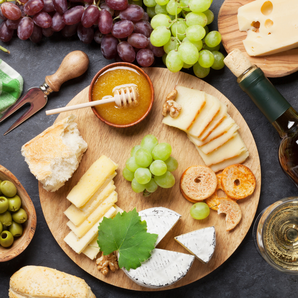 Сыр на столе с виноградом, оливками и белым вином