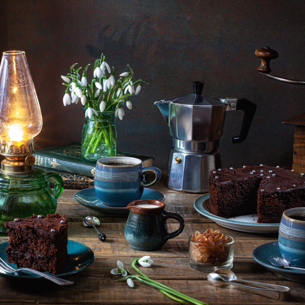 Шоколадный торт на столе с кофе, букетом подснежников и лампой