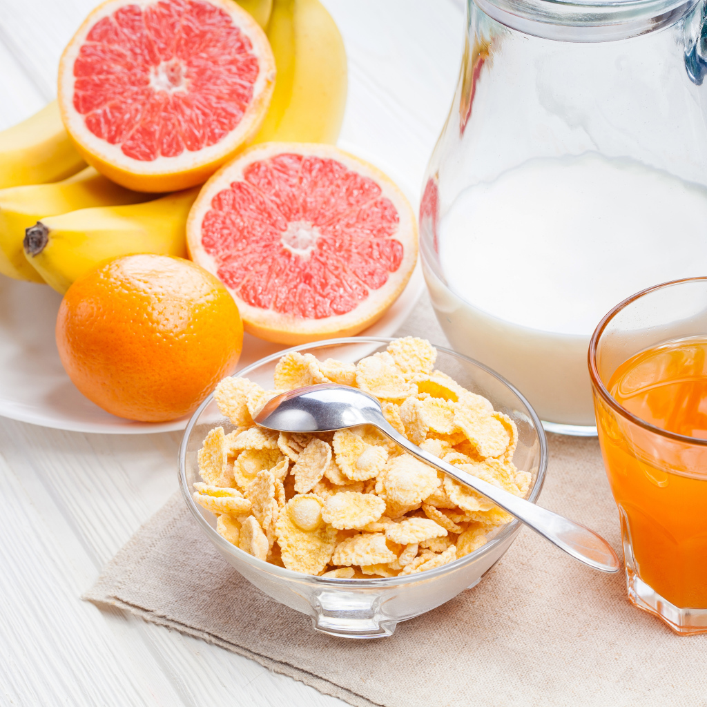 Кукурузные хлопья на столе с молоком, соком и свежими фруктами на завтрак