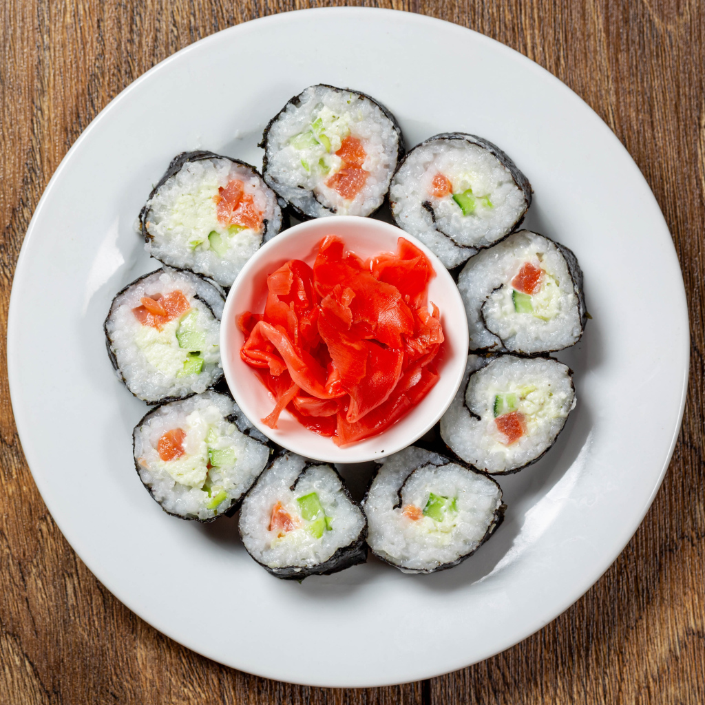 Вкусные суши на большой белой тарелке с имбирем