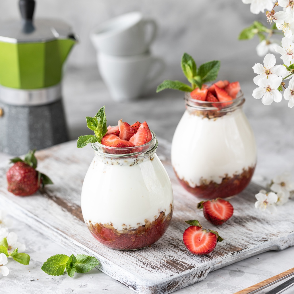 Десерт с йогуртом в банке с клубникой на столе цветами вишни 