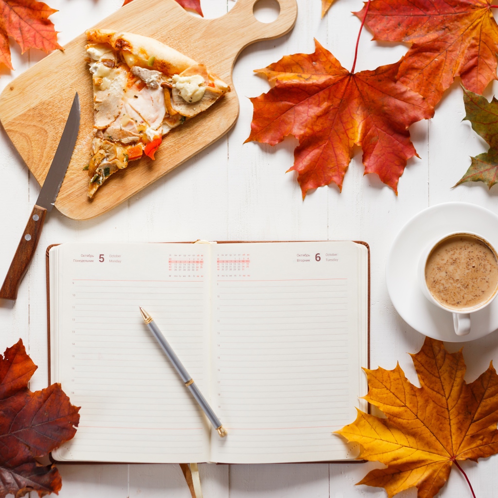 Ежедневник на столе с желтыми листьями, кофе и пиццей 