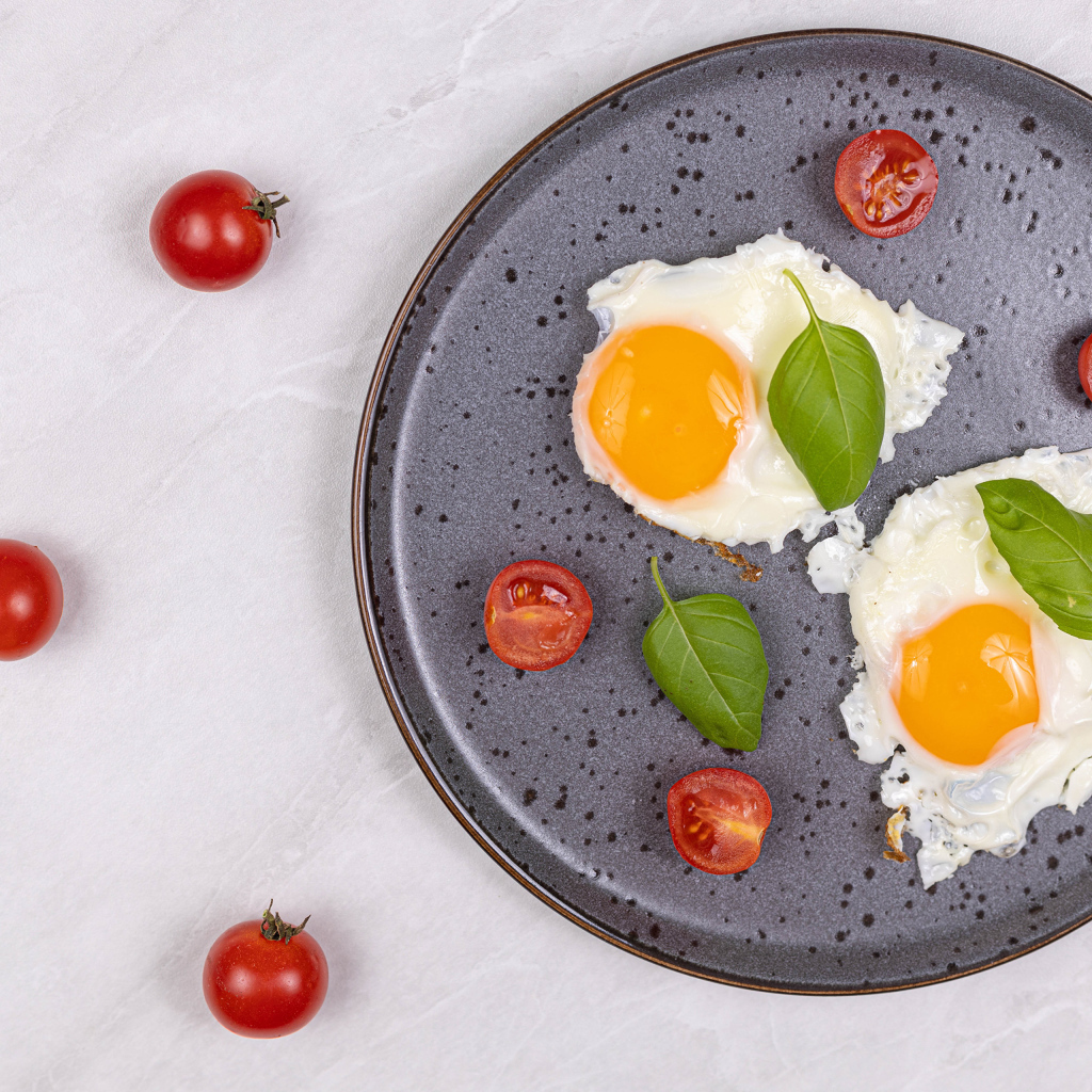 Яичница глазунья с помидорами и листьями базилика на черной тарелке 
