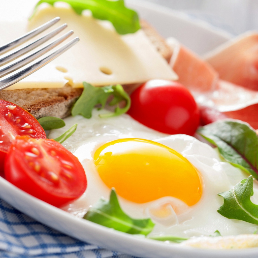 Fried eggs with tomatoes on a plate with ham and sandwich