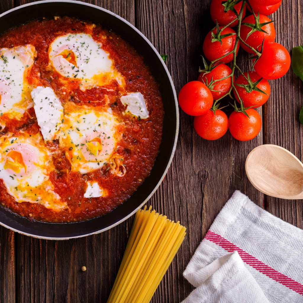 Греческое блюдо с томатами и яйцами на столе с спагетти и помидорами