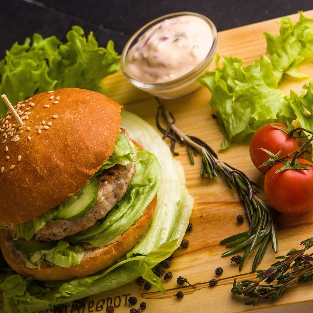 Гамбургер на столе с листьями салата, специями, помидорами и соусом