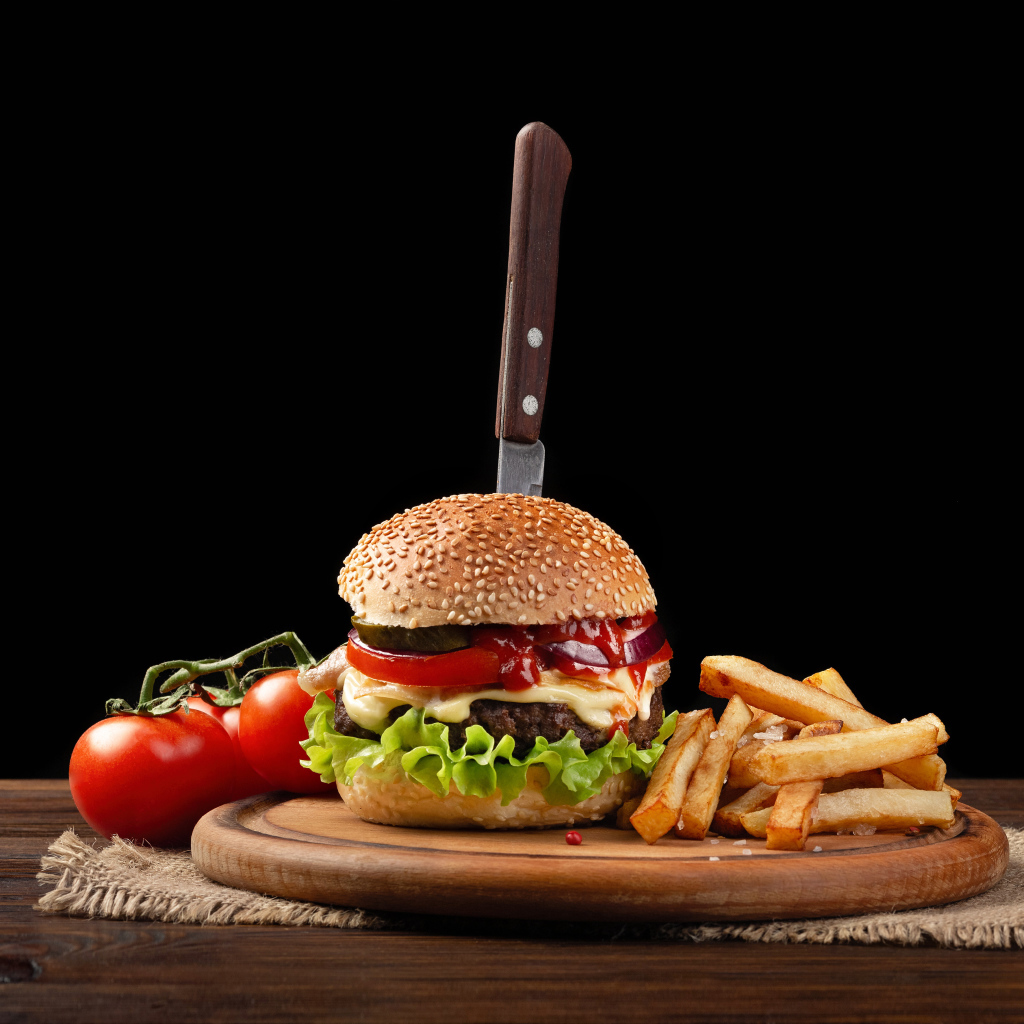 Hamburger with a knife on the table with tomatoes and fries