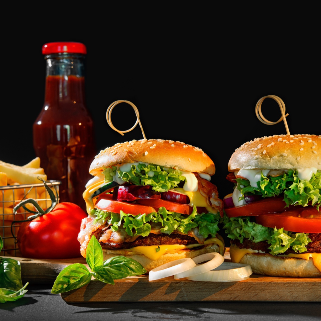 Гамбургеры на столе с картофелем и кетчупом на черном фоне