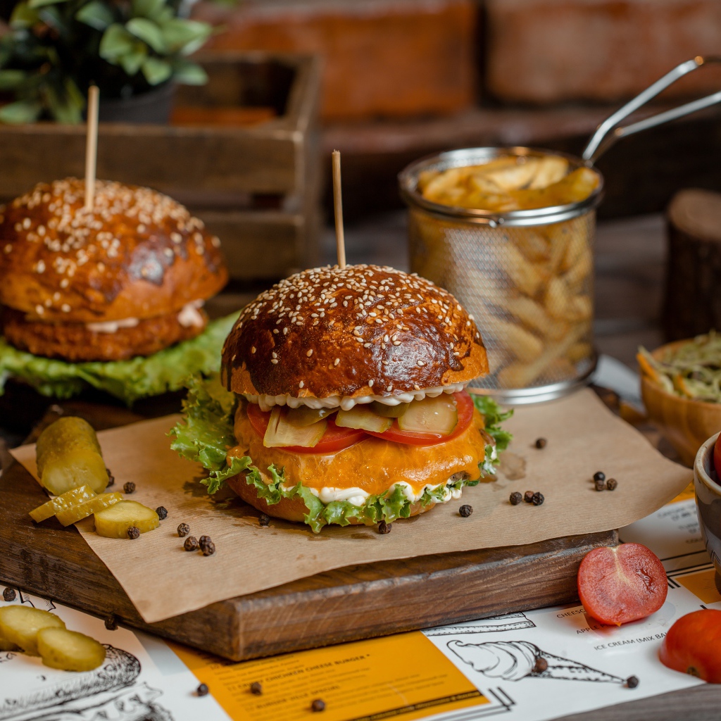 Гамбургеры на столе с помидорами, картофелем фри и солеными огурцами