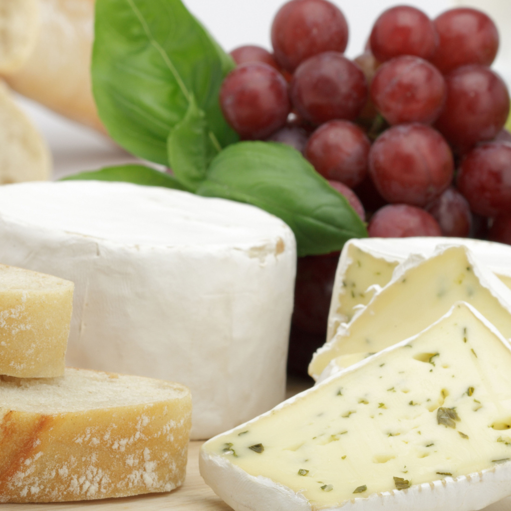 Твердый сыр на столе с батоном и виноградом