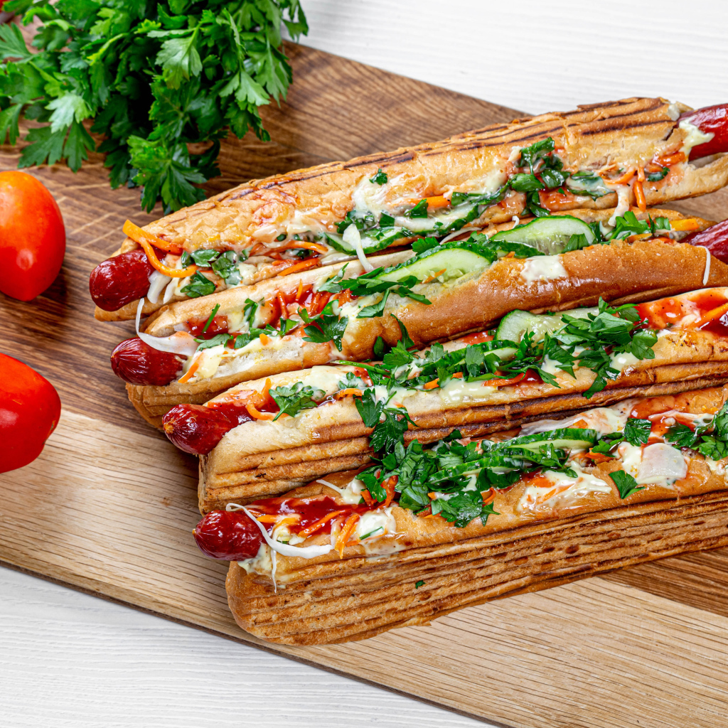 Hot dogs on a board with parsley and red tomatoes and parsley