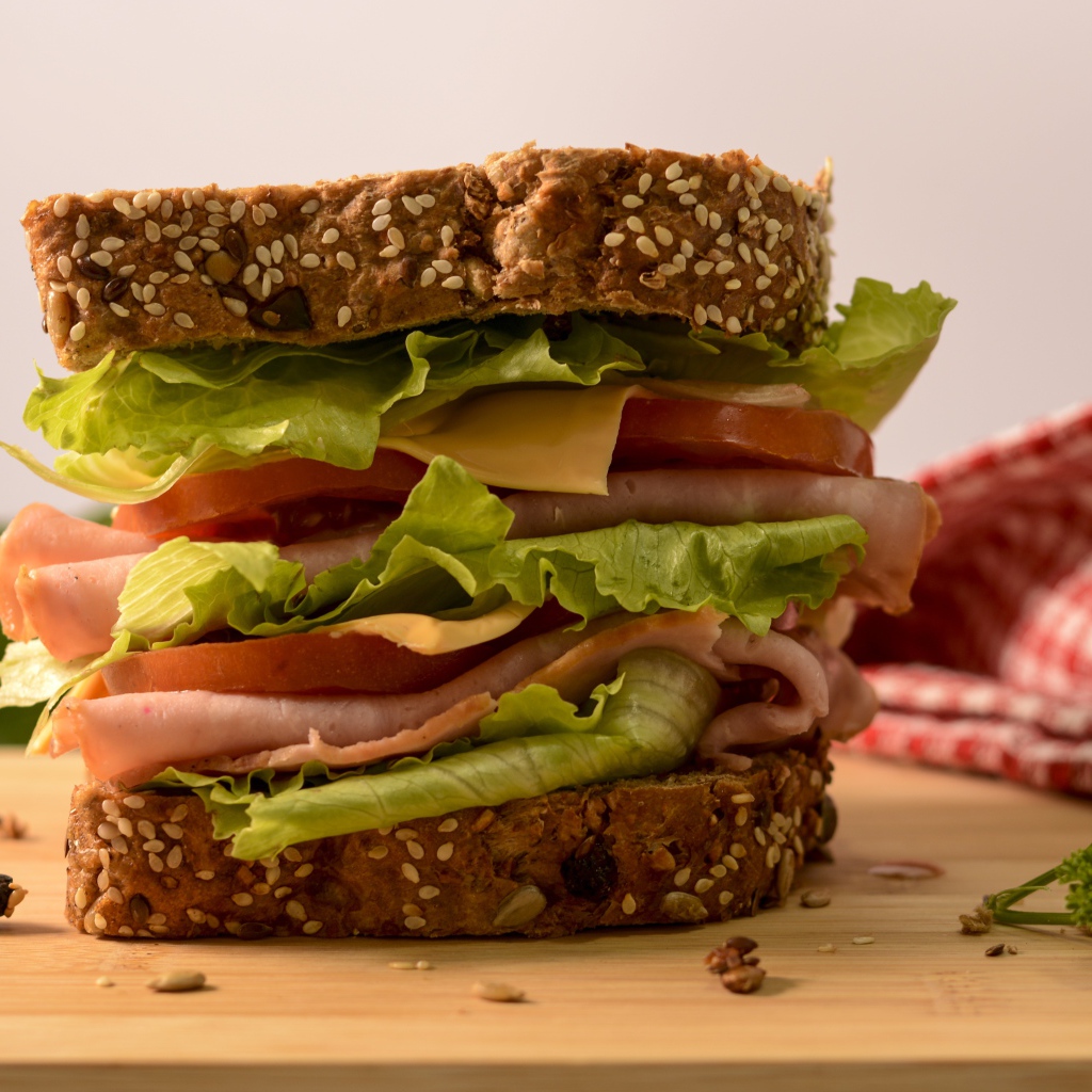 Большой бутерброд с ветчиной, сыром, помидорами и листьями салата 