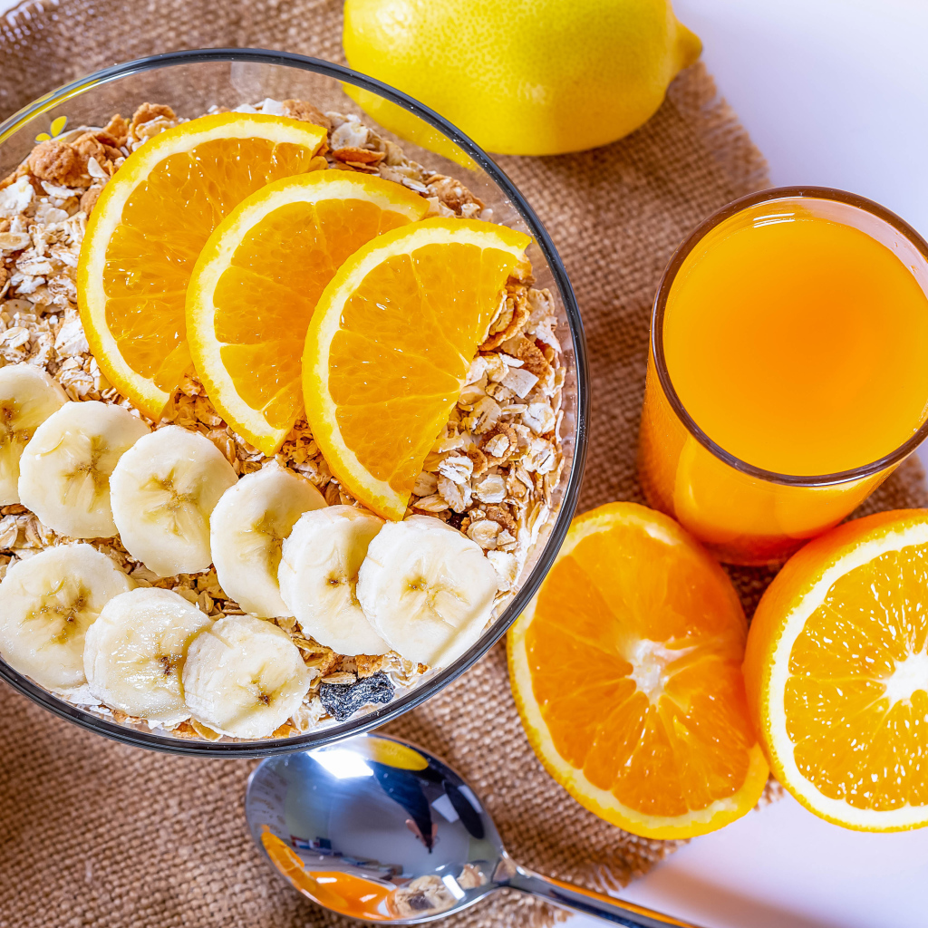Овсяные хлопья в тарелке с кусочками банана и апельсина на столе с соком