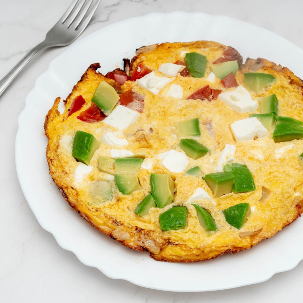 Омлет с авокадо и кусочками помидора на белой тарелке 