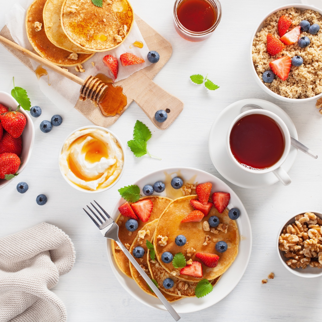 Оладьи с ягодами на столе с соком, чаем и мюсли на завтрак 