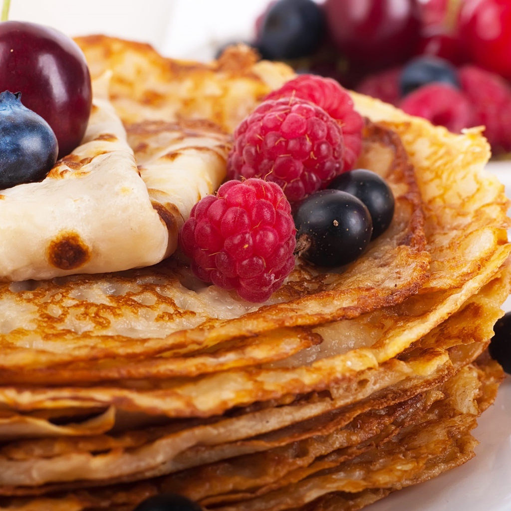 Блины с ягодами черники и малины на белой тарелке 