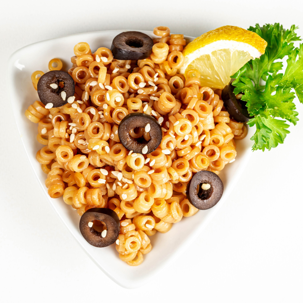 Макароны на тарелке с оливками и лимоном