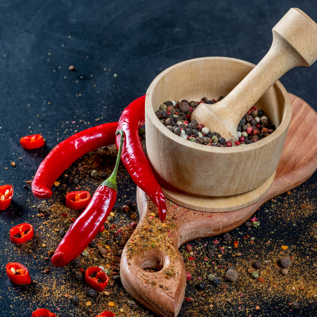 Peppercorns in a mortar on a table with hot pepper