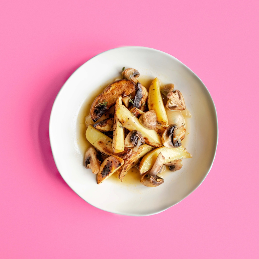 Картофель с грибами в тарелке на розовом фоне 