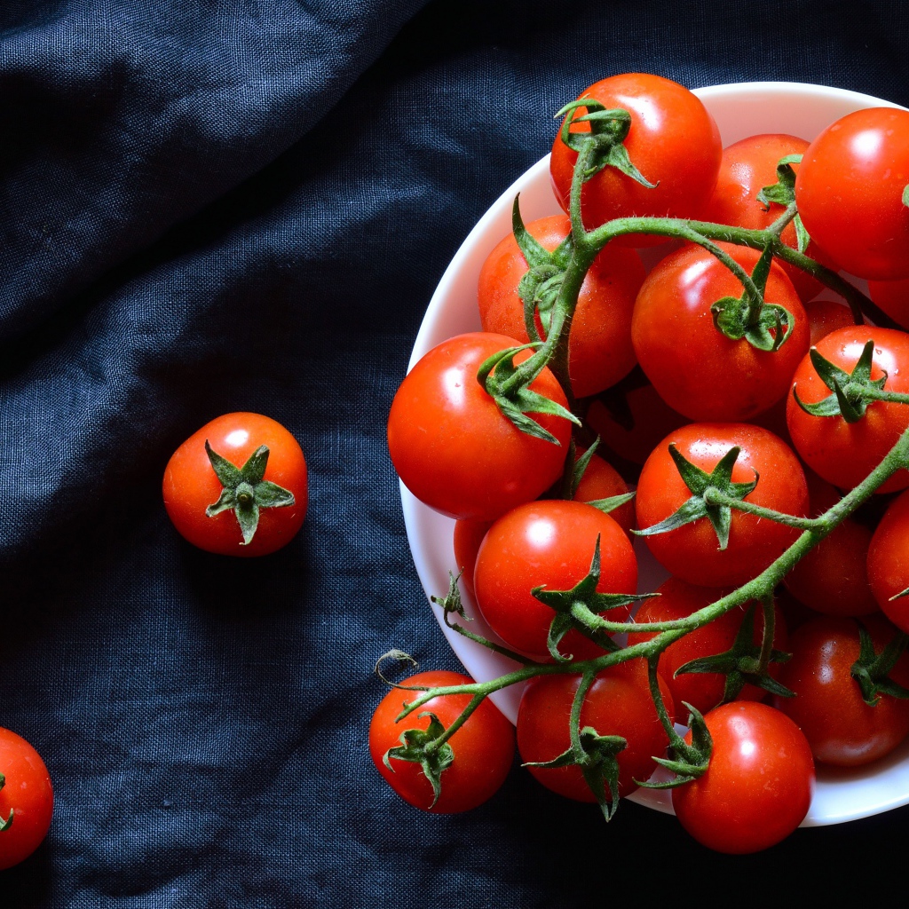 Красные помидоры в белой миске на черном фоне