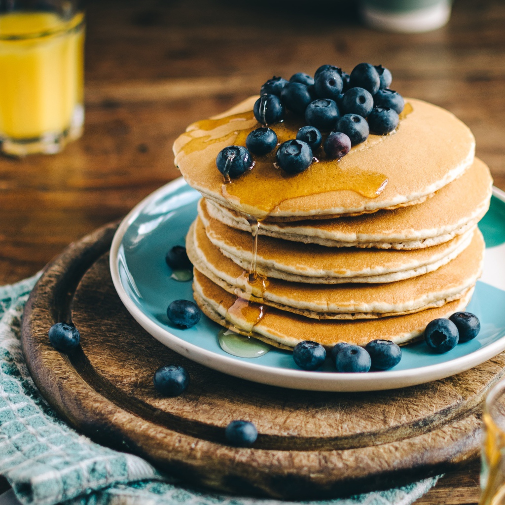 Румяные оладья на тарелке  с медом и ягодами черники 