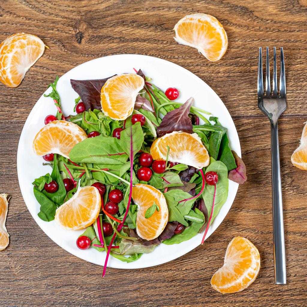 Салат из зелени и мандарина на белой тарелке на столе с вилкой