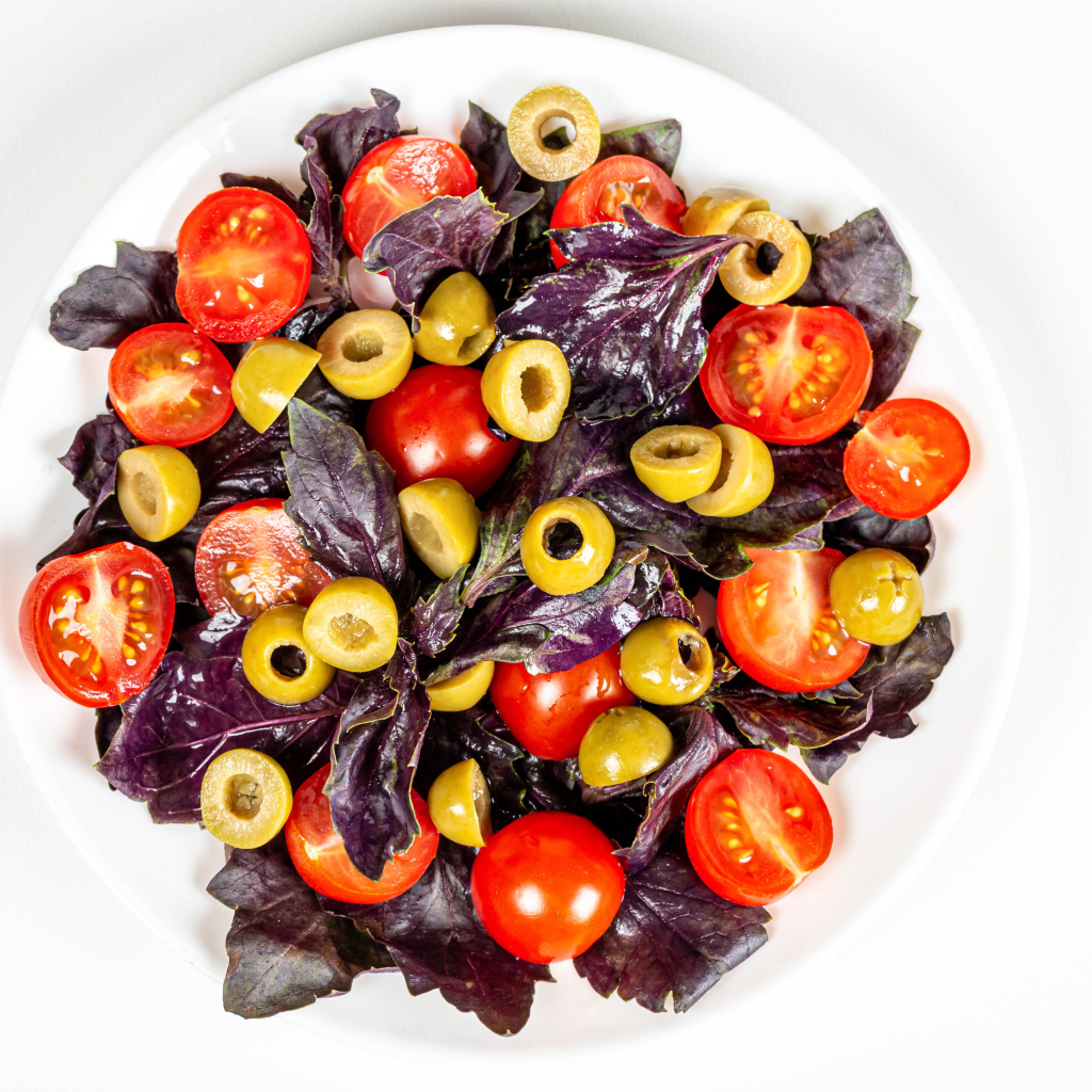 Салат с листьями базилика, помидорами и оливками на белом фоне