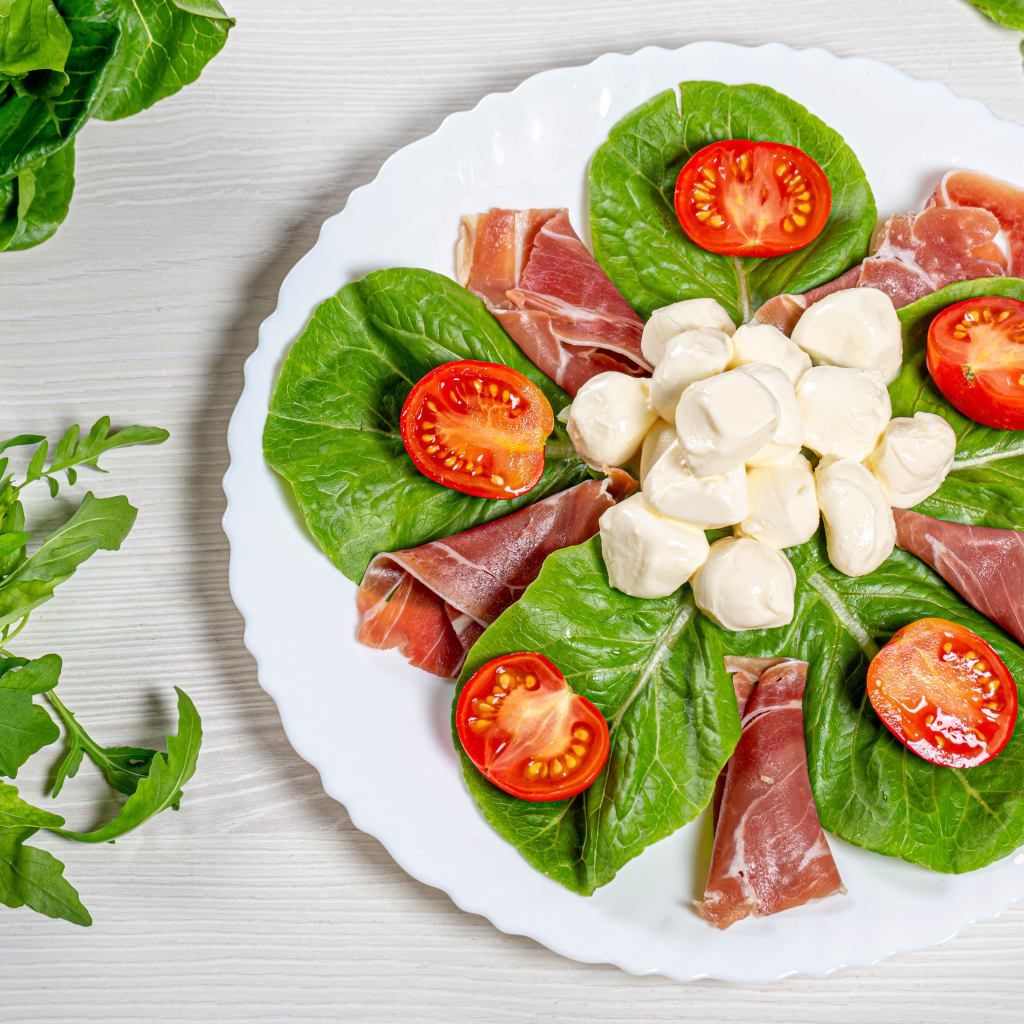 Кусочки ветчины на тарелке с сыром, помидорами и листьями салата