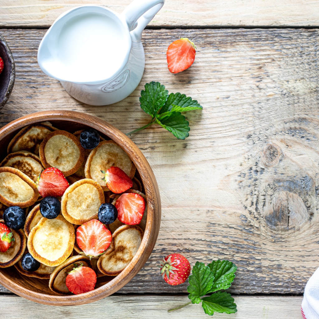 Маленькие оладьи в миске с клубникой и черникой на столе с молоком 