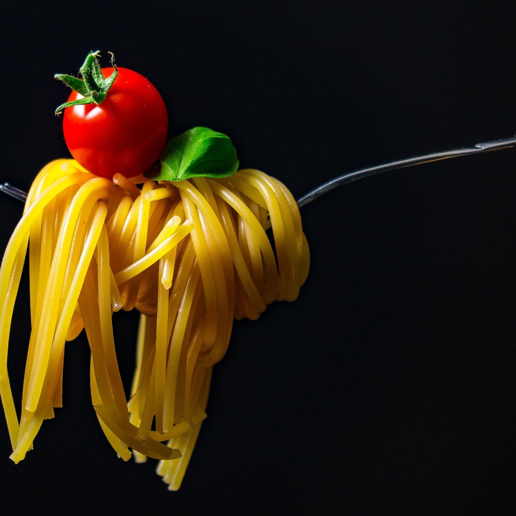 Спагетти с помидором на вилке на черном фоне