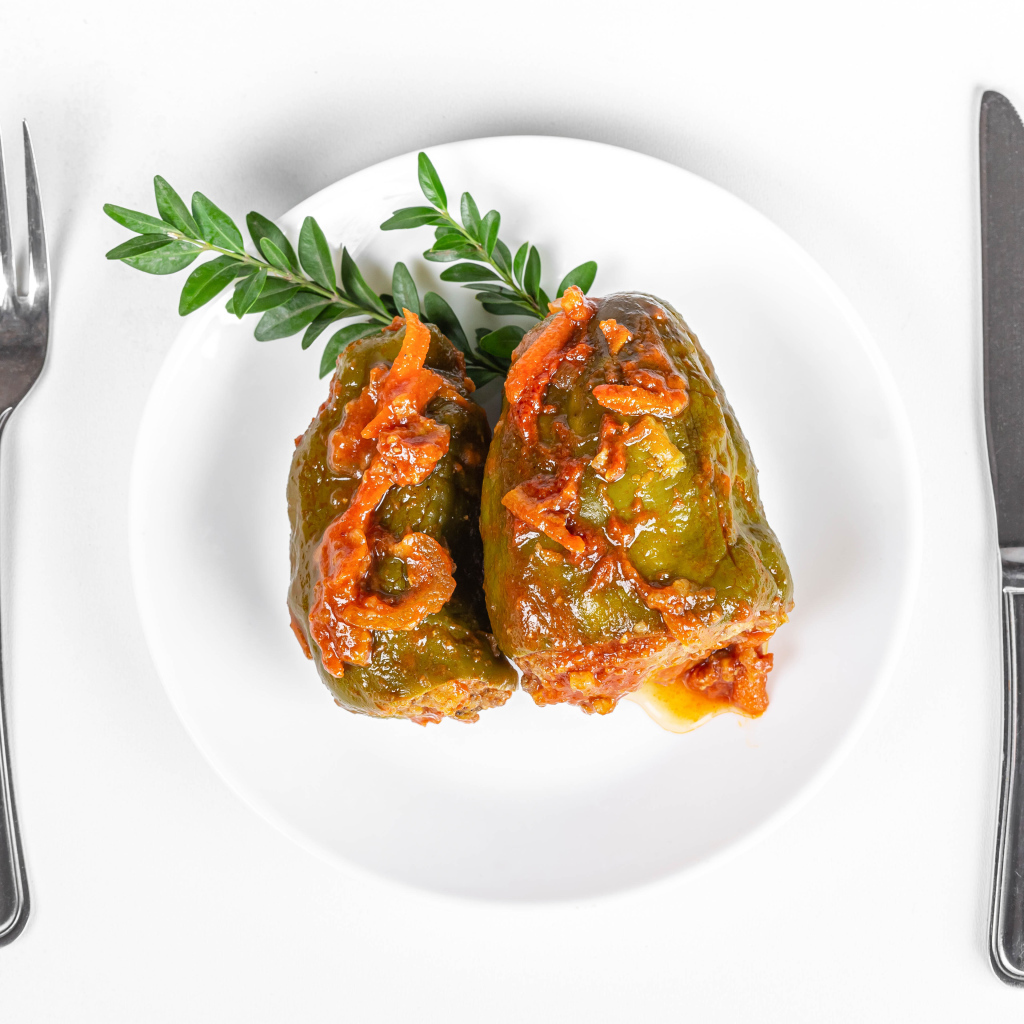 Фаршированный перец на белой тарелке со столовыми приборами