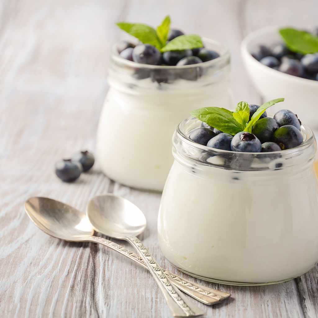 Йогурт в банках с ягодами черники на столе с ложками и медом