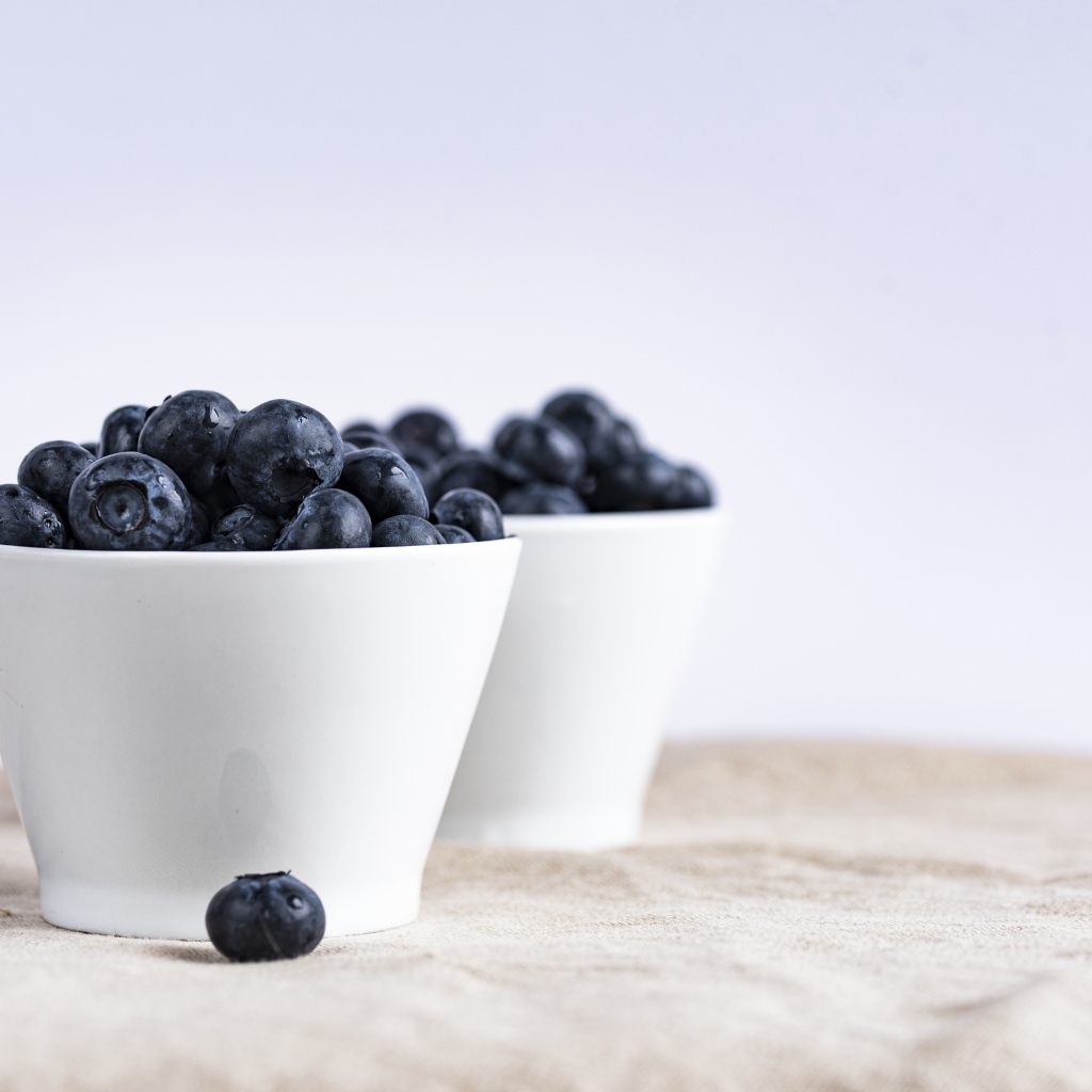 Синие ягоды черники в белой посуде на столе 