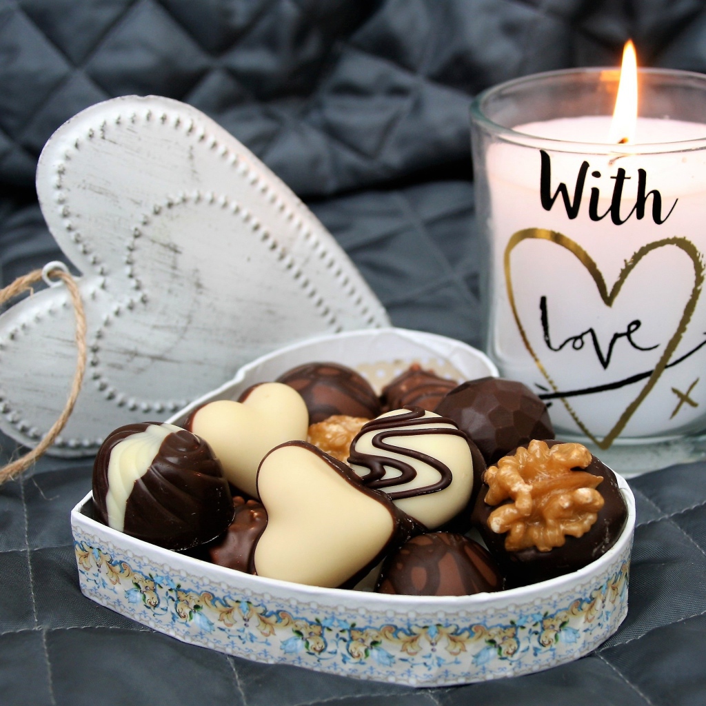 Chocolates in a heart shaped box on a bed with a lit candle