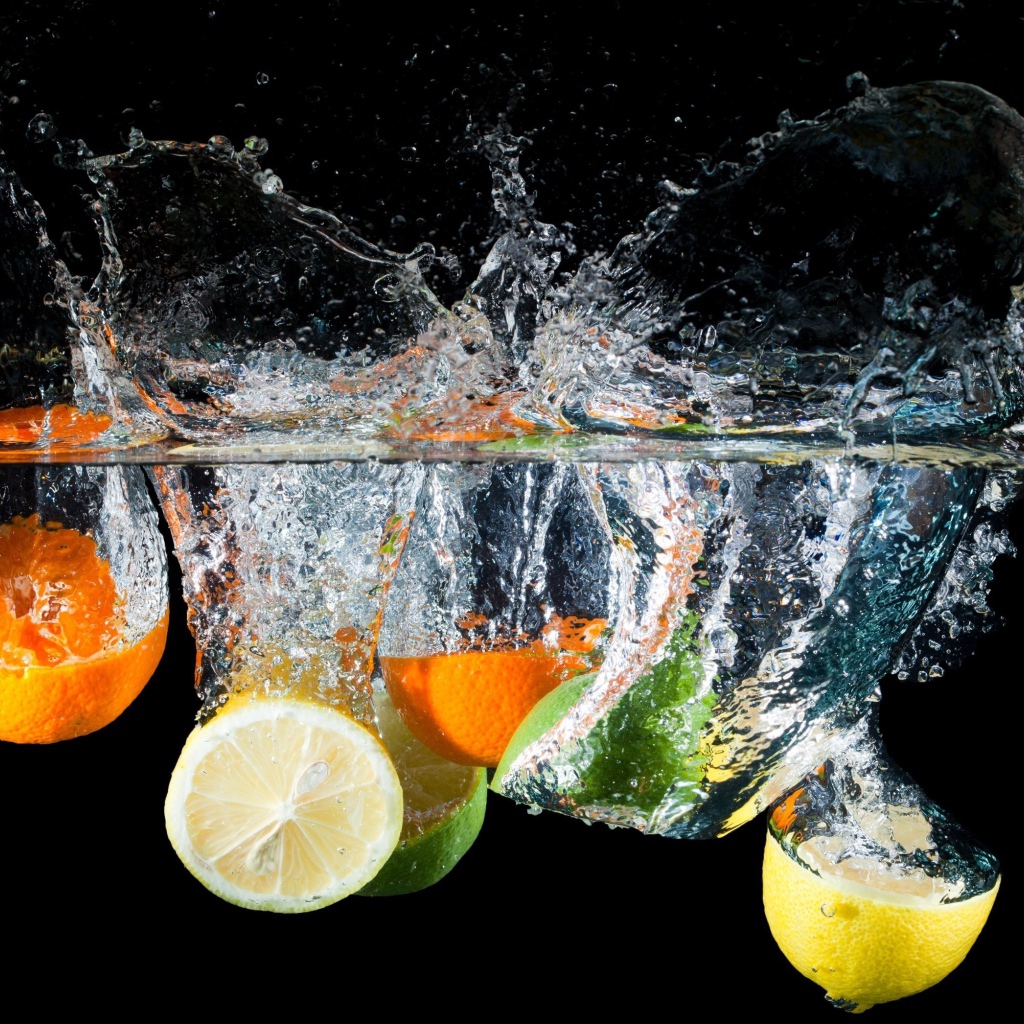 Цитрусовые фрукты падают в воду на черном фоне
